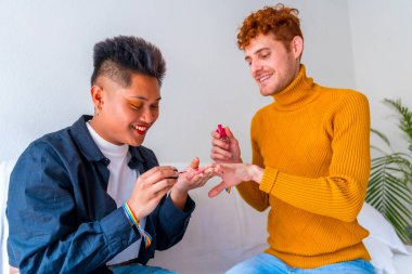 Güzel eşcinsel çift makyaj yapıyor, tırnaklarını boyuyor ve evde romantik bir şekilde gülümsüyor.