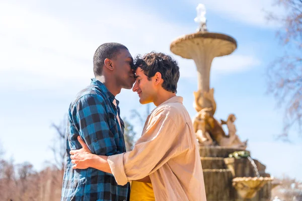 一对多种族的男人在一座城市的喷泉里 一个轻浮的概念 在一个浪漫的姿态上亲吻着对方的额头 — 图库照片
