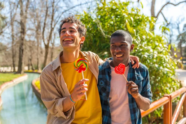 多种族的男同性恋夫妇在公园里吃棒棒糖和棒棒糖 开心地笑着 — 图库照片