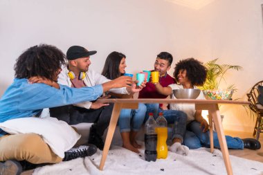 Bir grup arkadaş patlamış mısır yiyor ve meşrubat ile kadeh kaldırıyor. Evde televizyonda komik bir film izlerken gülüyorlar.