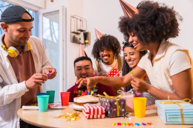 Doğum günü partisinde çok ırklı bir arkadaş grubu evdeki kanepede ellerinde pasta ve hediyelerle mumları yerleştiriyorlar.
