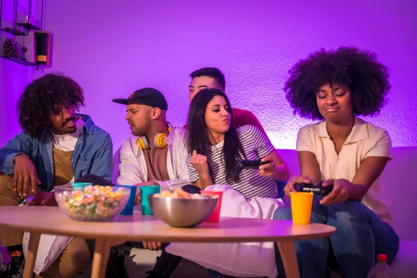 stock image Adult party. Young people sitting on the sofa playing video games with popcorn. Joystick or controller in hand, purple led, woman celebrating race victory