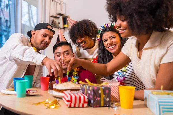 多民族の友人のグループは ケーキや贈り物を自宅でソファの上で誕生日パーティーで 幸せな誕生日のろうそくを置く笑顔 — ストック写真