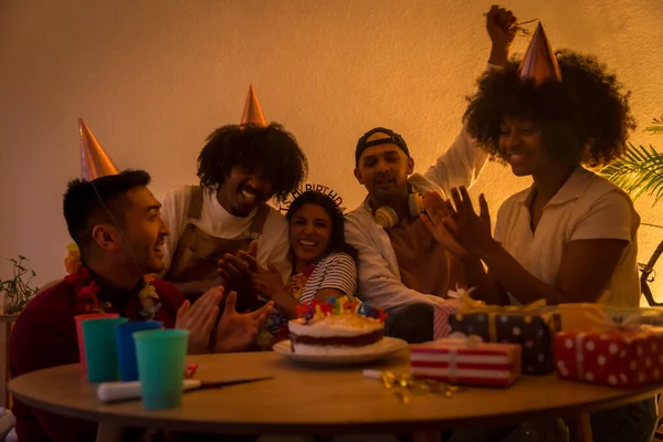 在家里的沙发上 一群多种族的朋友带着蛋糕和礼物参加了一个生日聚会 他们点着灯庆祝生日 — 图库照片
