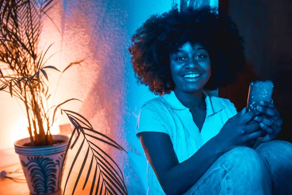 Afroamerykanka Afro Włosy Siedzi Domu Podłodze Patrząc Telefon Nocy Niebieskim — Zdjęcie stockowe