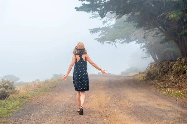 A tourist woman walking through the foggy path towards the juniper forest in El Hierro. Canary Islands