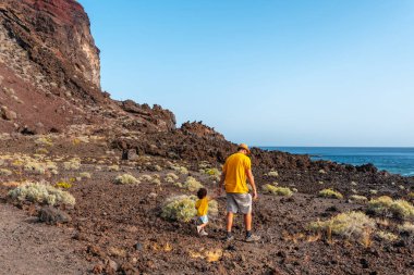 Oğluyla birlikte El Hierro, Kanarya Adaları 'ndaki Tacoron sahilinde volkanik bir yolda yürüyen bir baba.