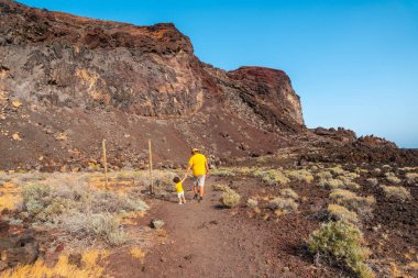 Oğluyla birlikte El Hierro, Kanarya Adaları 'ndaki Tacoron sahilinde volkanik bir yolda yürüyen bir baba.