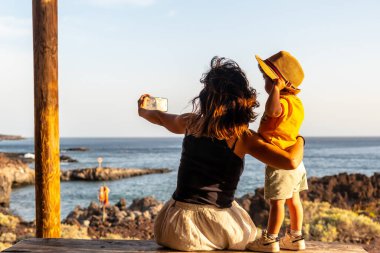 Anne ve oğlu tatilde. El Hierro, Kanarya Adaları 'ndaki Tacoron plajında fotoğraf çekiyorlar. Eğleniyor musun şapkalı çocuk?