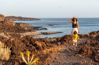 Anne ve oğlu gün batımında El Hierro, Kanarya Adaları 'ndaki Tacoron sahilinde yürüyor.