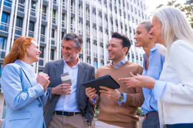 Ticari alandaki iş kadını, işkadını, işadamı ve yöneticilerin gülen ve açık hava tabletine bakan neşeli iş arkadaşları.