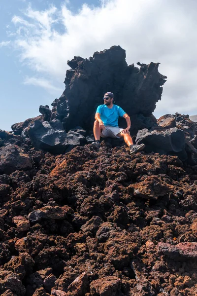 stock image Young tourist on the red stones on the volcanic trail in the village of Tamaduste on the coast of the island of El Hierro, Canary Islands, Spain. Throne of fire, throne of natural volcanic stones