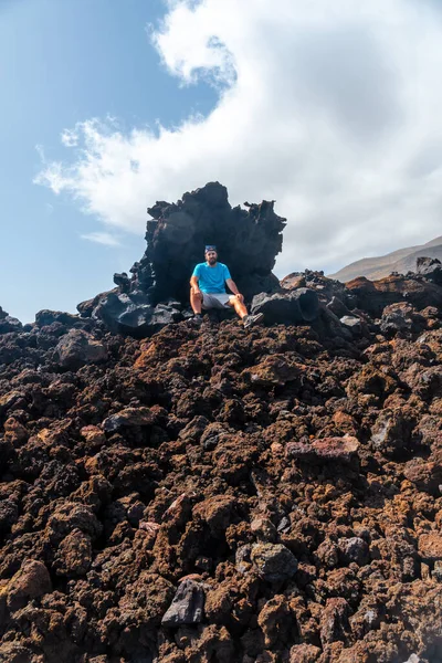 スペインのカナリア諸島エル ヒエロ島の海岸にあるタマドゥスト村の火山道の赤い石に座っている若い男 — ストック写真