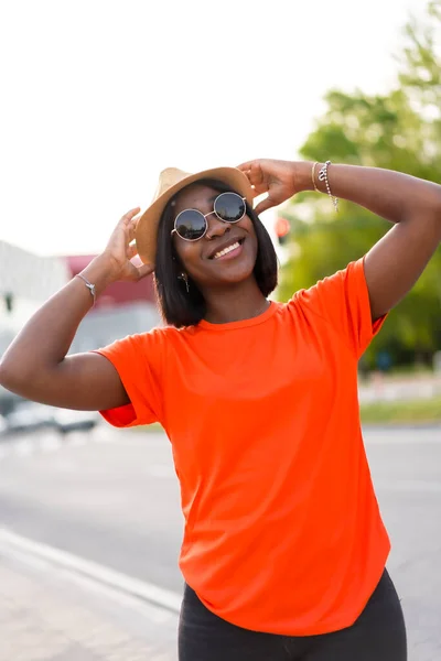 Leende Ung Svart Kvinna Med Solglasögon Och Hatt Bär Orange — Stockfoto
