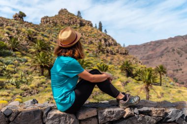 Şapkalı genç bir turist La Gomera, Kanarya Adaları 'ndaki El Palmarejo' nun manzarasının keyfini çıkarıyor.