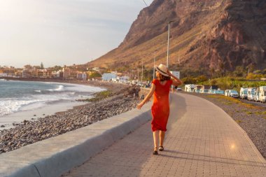 Gün batımında kadın turist La Gomera, Kanarya Adaları 'ndaki Valle Gran Rey kasabasının sahilinde yürüyor.