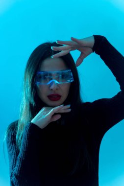 Metaverse teknoloji konsepti. Mavi arka planda kurşun ışığı olan fütürist gözlüklü bir kadın.
