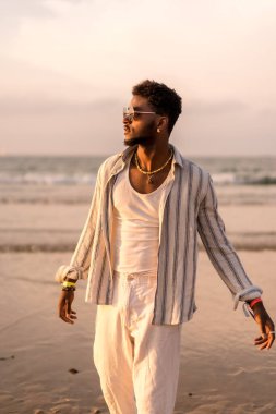 Siyah etnik adamın portresi gün batımında deniz kenarında yaz tatilinin tadını çıkarıyor.