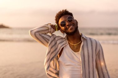 Siyah etnik modelin portresi deniz kenarında gülümseyen yaz tatilinin tadını çıkarıyor