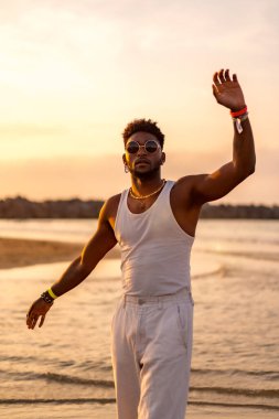 Siyah etnik köken modelinin portresi deniz kenarında güneş gözlüğü takarak yaz tatilinin tadını çıkarıyor.