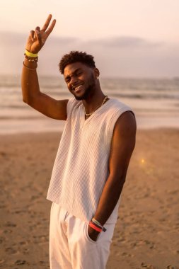 Siyah etnik köken modelinin portresi deniz kenarında tatilin tadını çıkarıyor, gülümsüyor ve deniz kenarında eğleniyor.