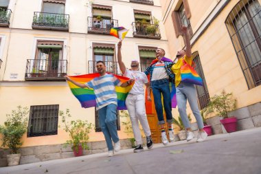 Homoseksüel erkek arkadaşlar gay onur partisinde sevinçten zıplıyorlar, şehirdeki gençlerin çeşitliliği, gökkuşağı bayraklarıyla gösteriye giden yol.