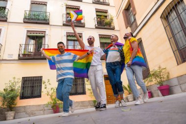Homoseksüel erkek arkadaşlar gay onur partisinde sevinçten zıplıyorlar, şehirdeki gençlerin çeşitliliği, gökkuşağı bayraklarıyla gösteriye giden yol.