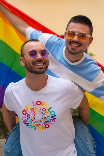 同性恋男性情侣骑在背上笑着参加带有彩虹旗的骄傲派对 — 图库照片