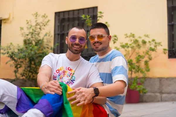 男同性恋夫妇坐在地板上 带着彩虹彩旗在傲慢派对上微笑的画像 — 图库照片