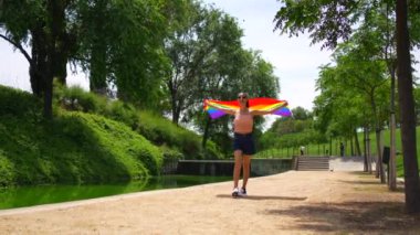 Parkta yürüyen LGBT bayrağıyla beyaz esmer bir kadın. Özgür ve cinsel tercihleriyle gurur duyan lezbiyen bir kadın.