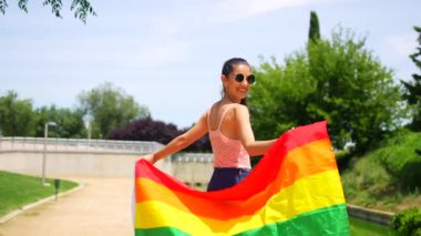 Parkta yürüyen siyah LGBT bayrağıyla beyaz esmer bir kadın. Lezbiyen bir kadının gülümsemesi.