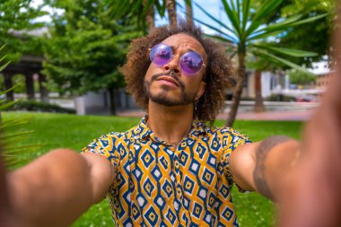 Yaz tatilinde, plajın yanındaki palmiye ağaçlarının yanında Afro saçlı bir adam iki eliyle selfie çekiyor. Seyahat ve turizm kavramı