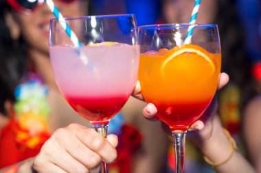 Bir gece kulübünde kadeh kaldıran ve bir gece partisinde gülümseyen kadın arkadaşlar.