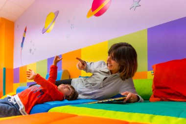 Kadın öğretmen, bir anaokulunun içinde, bir kitapla oynamayı öğretiyor.