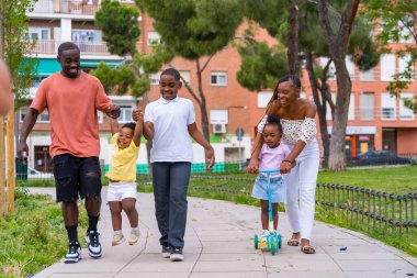 Çocuk parkında çocukları olan Afrikalı siyahi etnik aile, şehir parkında eğleniyor.