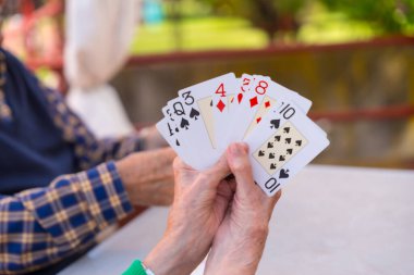 Huzurevinin bahçesinde iki yaşlı insanın elleri ya da bir yaz sabahı kart oynayan huzurevi.