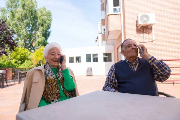 Huzurevinin bahçesindeki iki yaşlı insan telefona bakıyor, yaşlılarda teknoloji var.