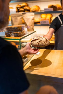 Fırındaki müşterinin elleri atölyedeki fırından zanaatkar ekmeği alıyor, dikey fotoğraf.