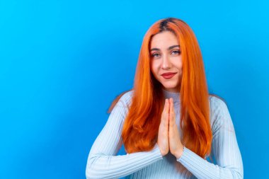 Stüdyo fotoğrafçılığındaki kızıl saçlı kadın jestini mavi arka planda yapıyor.