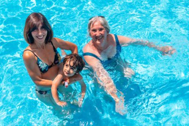 Anne ve büyükanne yaz tatilinde yüzme havuzunda torunlarıyla eğleniyorlar.