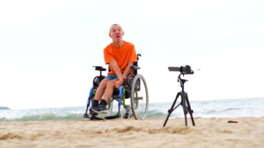 Plajda tekerlekli sandalyede sakat bir insanın portresi bir video blogu kaydediyor.