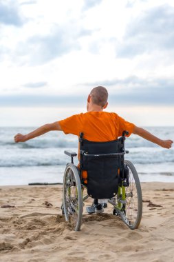Sahilde tekerlekli sandalyede sırtüstü yatan engelli biri.