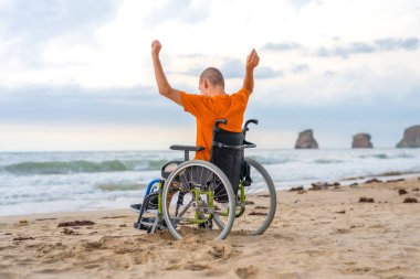 Tekerlekli sandalyede sırtüstü yatmış, kollarını açıp denizin ve doğanın özgürlüğünün tadını çıkaran engelli bir adam.