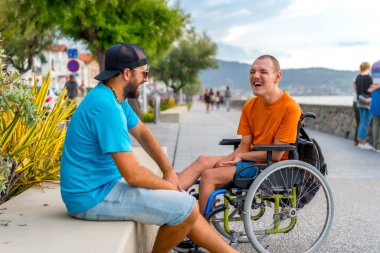 Tekerlekli sandalyede bir arkadaşıyla yaz tatilinde olan engelli biri çok eğleniyor.