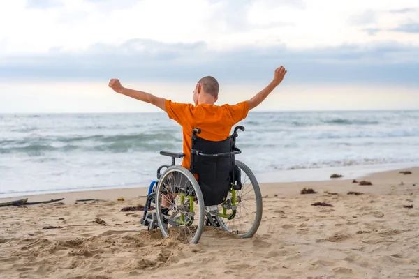 stock image Disabled person on his back in a wheelchair on the beach with open arms enjoying the freedom