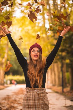 Portrait of a woman in autumn in a forest with brown leaves at sunset in a city park, throwing leaves