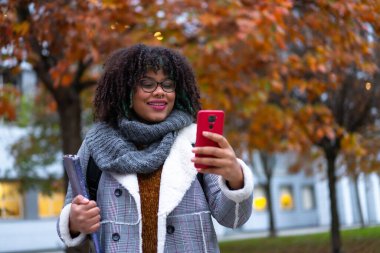 Portrait of black ethnic girl walking in college college in autumn talking on phone back to school