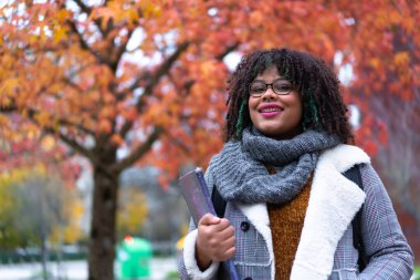 Portrait of black ethnic girl strolling in university college under fall foliage trees on back to school