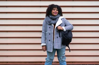 Portrait of black ethnic girl a gray wall in the university, with mochica from school on the back to school