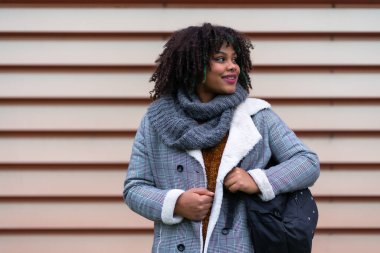Portrait of black ethnic girl a gray wall in the university, with a schoolgirl on the back of the school, looking to the right